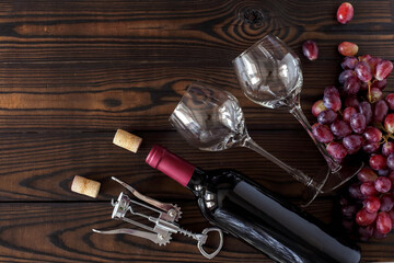 top view of glasses and a bottle of red wine, a bunch of ripe grapes on a dark wooden table. horizontal layout with space for text