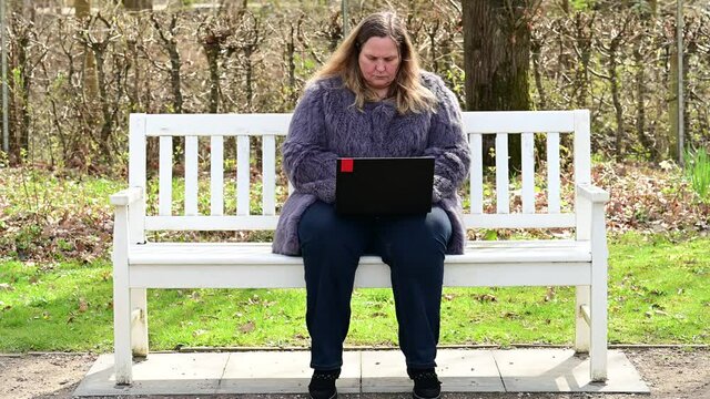 Frau in einer Kaninchenfell Jacke arbeitet im Garten mit einem Notebook im Homeoffice  