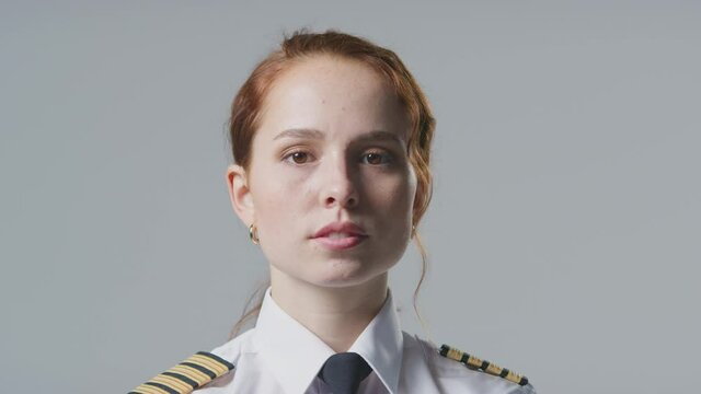 Serious young female airline pilot or ship captain wearing uniform in front of plain studio background - shot in slow motion