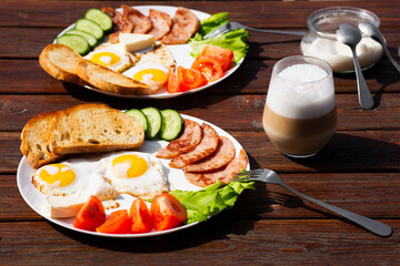 Continental breakfast set of eggs, ham, vegetables and cheese. Bread and coffee on a wooden table. Breakfast for two outside on a sunny summer day.