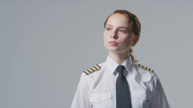 Serious young female airline pilot or ship captain wearing uniform looking off camera in front of plain studio background - shot in slow motion