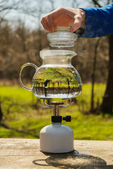 Glass kettle filled with water and heated on a camping gas burner. The lid is removed from the kettle to add tea.