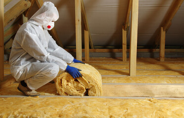 Worker thermally insulating house attic with glass wool