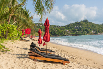 Fototapeta na wymiar Tropical sand beach with wooden deck chairs and umbrellas near sea on a sunny day. Nature concept. Thailand