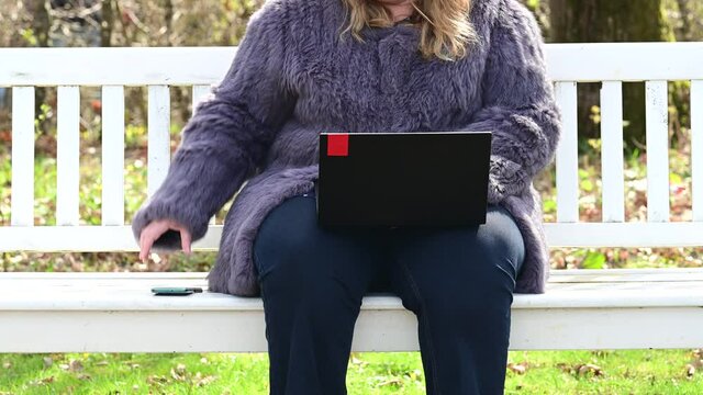 Frau in einer Kaninchenfell Jacke arbeitet im Garten mit einem Notebook im Homeoffice  