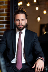 Portrait of beautiful man’s long curls hair. Happy young businessman, dress in jacket, shirt and tie, sitting and posing. 