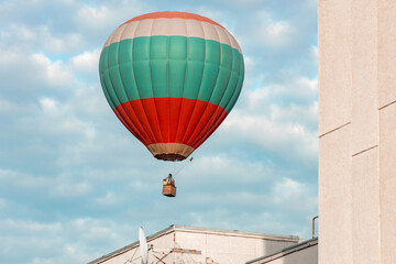Fototapeta na wymiar a balloon flies out from behind a building, a low flying balloon with a basket and people