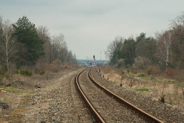 Tory kolejowe prowadzące w kierunku odległej stacji kolejowej. - obrazy, fototapety, plakaty