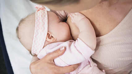 mother feeding with breast baby girl in headband with bow.