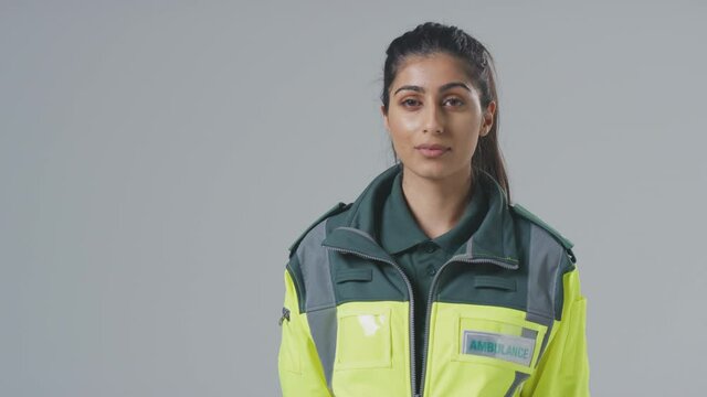 Serious young female paramedic wearing uniform in front of plain studio background - shot in slow motion
