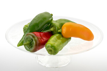 Pointy peppers on clear glass raised plate. Red, yellow and green peppers isolated on white