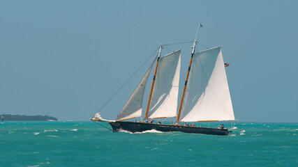 Naklejka premium Sailboat or Sail yacht with American flag. Private cruise tour. Summer vacations on ocean or Gulf of Mexico Florida. Yachting sport. Turquoise ocean color. Beautiful seascape. 