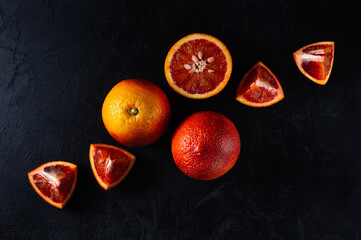 red oranges, whole and cut, lie diagonally on a black concrete background. artistic moody fruit concept photo
