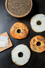 Pattern design of bagels with sesame seeds and poppy seeds and soft white cream cheese. Top view. Black stone texture background