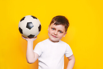A little cute boy in a white t-shirt with a soccer ball in his hand smiles  isolated on a bright...