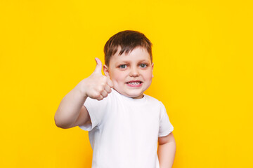 Portrait of a little caucasian happy smiling kid boy in a white t-shirt showing thumb up like...