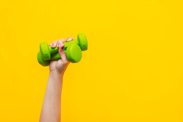 Fototapeta na wymiar Two green dumbbells in a woman's hand isolated on a bright color yellow background. Sport equipment. Fitness concept, healthy lifestyle. Copy space for design