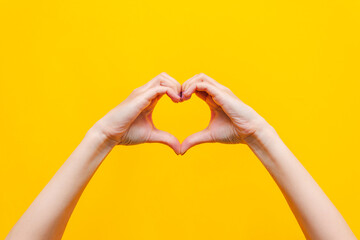Female hands showing a heart shape isolated on a bright color yellow background. Sign of love,...