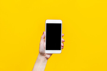 Fototapeta na wymiar Template for the design. White phone with black screen in female hand isolated on a bright color yellow background. Black blank with an empty copy space for the text. Mockup of a smartphone