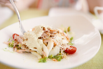 Fork in white plate with salad. Lunch break menu. Salad with eggs, lettuce, cherry tomatoes, chicken and cheese. Healthy food.