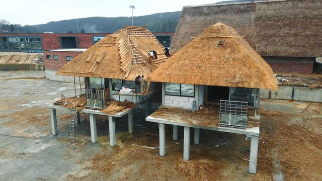 Aerial view Construction of a holiday home from hay and straw. Workers who equip the roof of the house with dry straw.