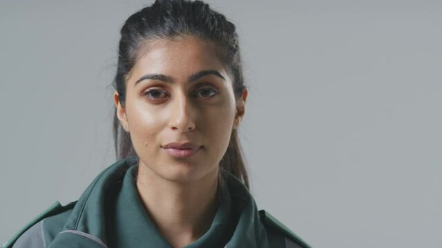 Close up of serious young female paramedic wearing uniform in front of plain studio background - shot in slow motion