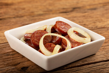 Sliced ​​calabrese sausage with onion on wooden background.