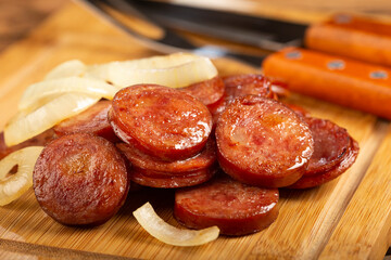 Sliced ​​calabrese sausage with onion on wooden background.