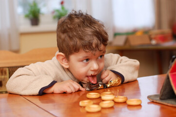 Little boy enjoys eating chocolates and watching cartoons on the tablet at home. Chocolate gives a...