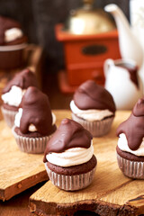 Chocolate cupcakes with cherries, cream and chocolate icing. Side view. Wooden background.
