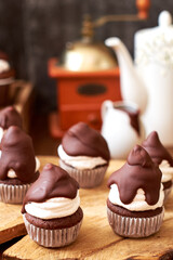 Chocolate cupcakes with cherries, cream and chocolate icing. Side view. Wooden background.