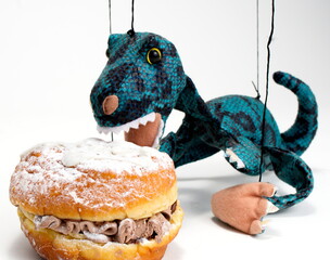 A puppet T-Rex dinosaur sitting down to eat a tasty, cream filled donut.