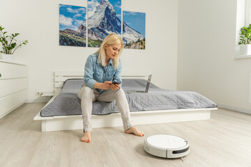 Robotic vacuum cleaner cleaning the room while woman controlling vacuum with remote control.