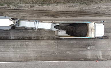 Aerial. Road repair using special equipment. The machine cuts off the top layer of the old asphalt and dumps it into the truck. Top view from drone.