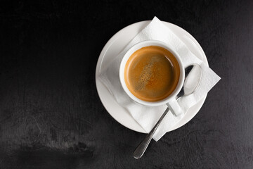 Close up white cup full of black instant coffee with froth on porcelain saucer over brown paper background, close up, elevated top view, directly above