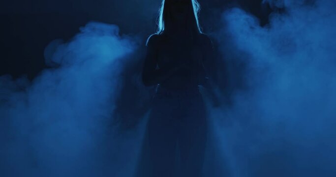 Mysterious night haze and female silhouette in neon blue light. 4k video of woman and smoke