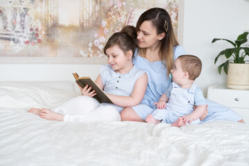 Fototapeta premium mother reads a book with two children baby son and little girl daughter in bed