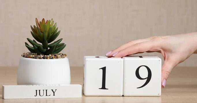 Wooden calendar with an important event for July 19, a woman's hand sets the date on the calendar. Summer season.

