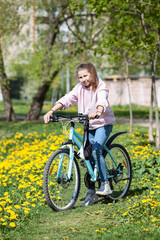 Fototapeta na wymiar Portrait of teenager Caucasian girl standing with bicycle in spring park with yellow flowers