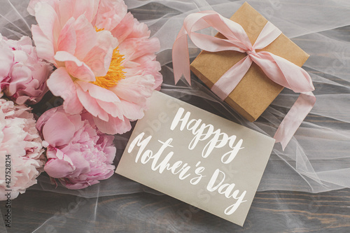 Happy mother's day. Happy mother's day text on card and beautiful peony bouquet, gift box on soft tulle on dark wood. Stylish floral greeting card. Handwritten lettering. Mothers day