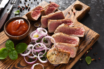 Grilled beef steak with onions and sauce on a wooden board. Fried meat slices.