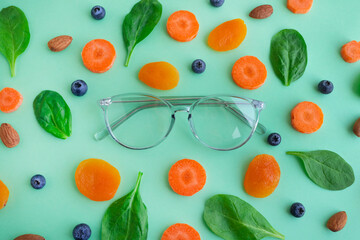 Glasses and products for improving vision, spinach, dried apricots, blueberries, almonds and carrots on a green background, top view.