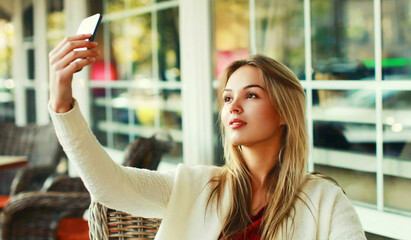 Close up of young woman taking selfie picture by smartphone sitting at a table in a cafe