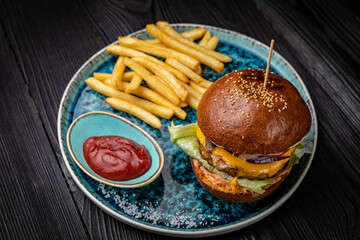 Hamburger with french fries and sauce on a dark wooden table
