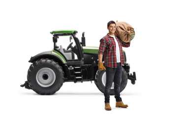 Full length portrait of a male farmer holding a sack in front of a tractor