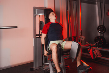 Fototapeta na wymiar a young man is engaged in leg training while sitting on a simulator in the gym