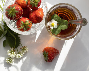 Cup of tea and wild strawberries on a white lace background