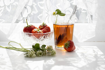 Cup of tea and wild strawberries on a white lace background