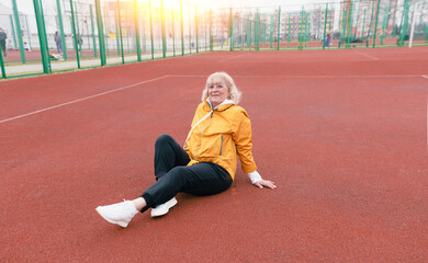 an elderly woman sits and rests after a workout on a red treadmill.