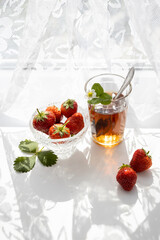 Cup of tea and wild strawberries on a white lace background